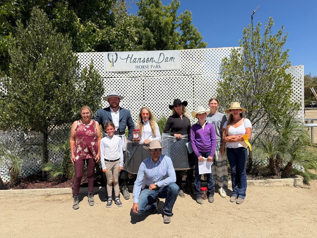 Riders and families with ribbons and prizes in front of the Hansen Dam Horse Park sign
